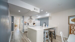 A modern kitchen with a central island, bar stools, and a dining table. - The Salty Seahorse | Pet-Friendly Canal Retreat w/ Grill & Deck (Rockport)
