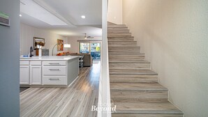 A modern kitchen with white cabinetry, a central island, and a view to the living area. - The Salty Seahorse | Pet-Friendly Canal Retreat w/ Grill & Deck (Rockport)