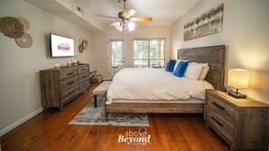 A bedroom with a bed, wooden dresser, nightstand, and a ceiling fan. - Meet Me at the Lake - Gated Staycation Hideaway (Lago Vista)
