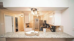 A kitchen with granite countertops, white cabinets, a built-in oven, and a coffee maker. - Meet Me at the Lake - Gated Staycation Hideaway (Lago Vista)