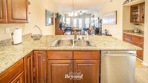 A kitchen with granite countertops, wooden cabinets, a stainless steel sink, and a built-in dishwasher. - Lakeview & Pool View on an Island with Sauna & Spa (Lago Vista)