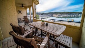 A wooden table and chairs on a balcony with a view of a river and distant hills. - Lakeview & Pool View on an Island with Sauna & Spa (Lago Vista)