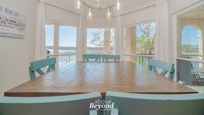 A dining area with a wooden table and turquoise chairs, large windows offering a view of the outdoors, and a chandelier with multiple bulbs.