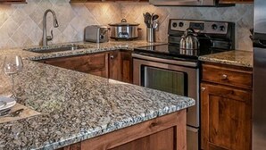 A kitchen with wooden cabinets, granite countertops, a stainless steel microwave, a stove, and a sink. - Spring Break in Breckenridge! Ski in/out on Peak 7 (Breckenridge)