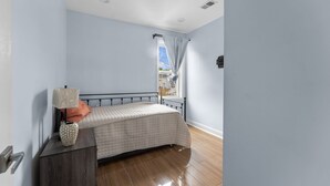 A bedroom with a bed, a nightstand, a lamp, a window with curtains, and a view of buildings outside.