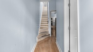 A narrow hallway with a wooden staircase leading to a kitchen area.