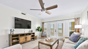 A living room with a flat-screen TV, wooden coffee table, sofa, and a ceiling fan. - Island Summer Sunrises | Spa | Eats | Last Minute Deals! (Lago Vista)
