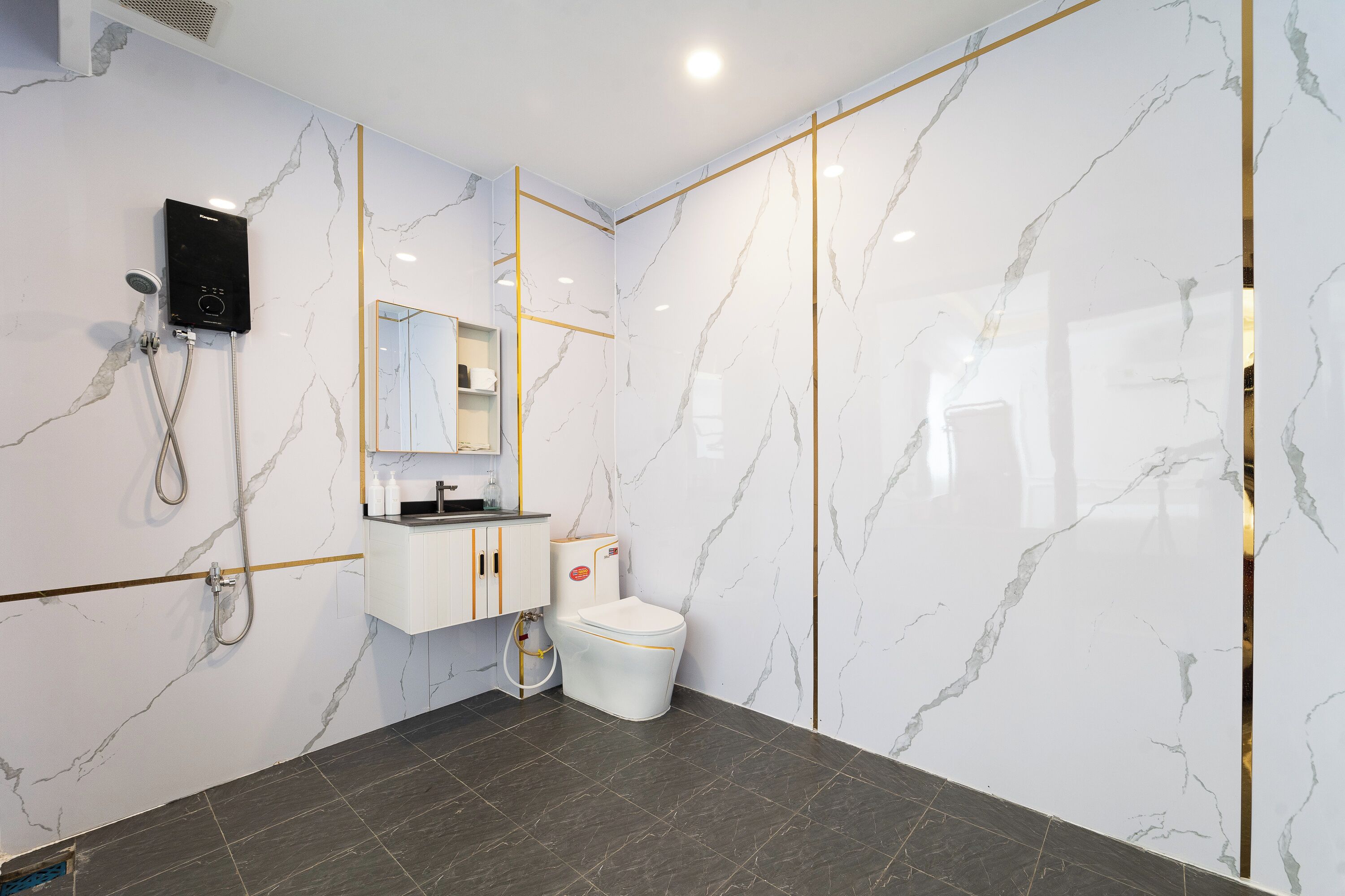 A modern bathroom with a white marble wall, a black floor, a white toilet, a sink with a mirror, and a shower unit.