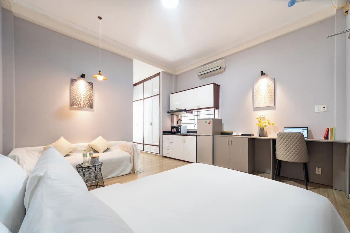 Quarto de hotel moderno com uma cama grande, uma escrivaninha e uma cozinha compacta.