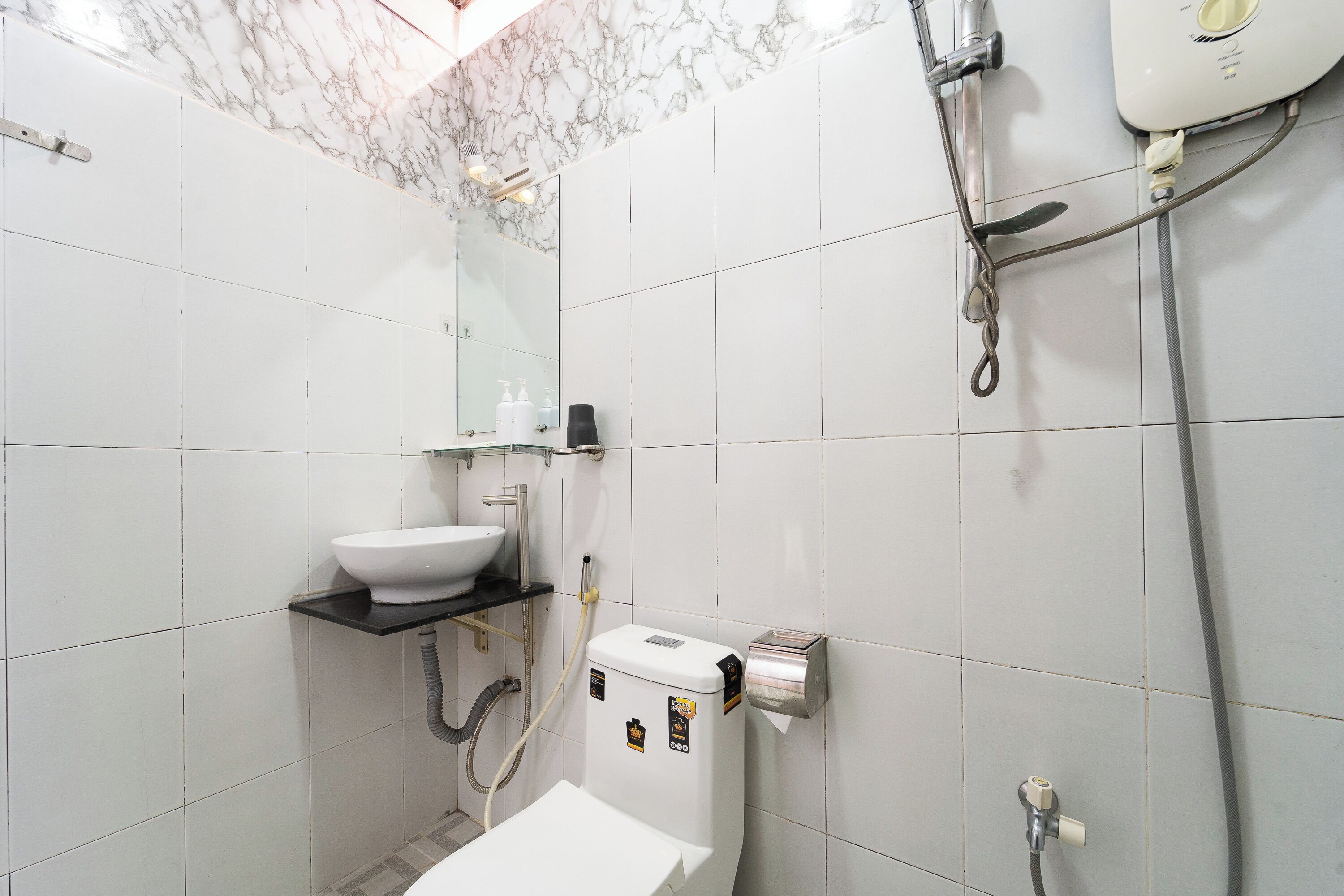 Une salle de bain avec des carreaux blancs, un lavabo blanc, des toilettes, un miroir et un espace douche.