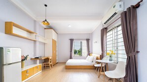 Ein gemütliches Hotelzimmer mit Bett, Schreibtisch, Stuhl, einem kleinen Tisch mit Blumenvase und einem Kühlschrank.