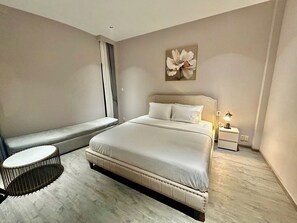 Une chambre à coucher moderne avec un grand lit, un banc près de la fenêtre et une petite table ronde.