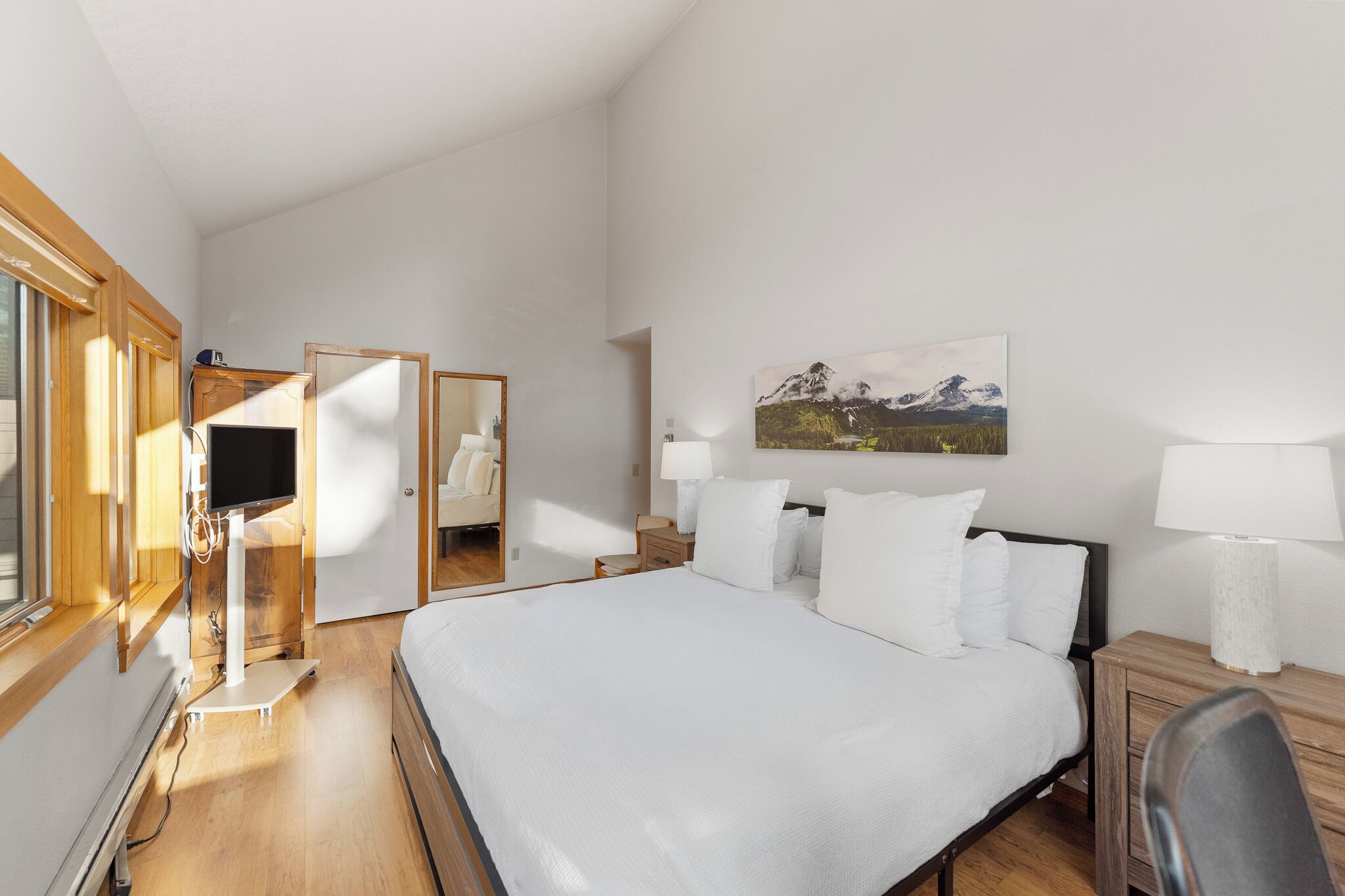 A bedroom with a bed, bedside lamps, a TV, and a painting on the wall.