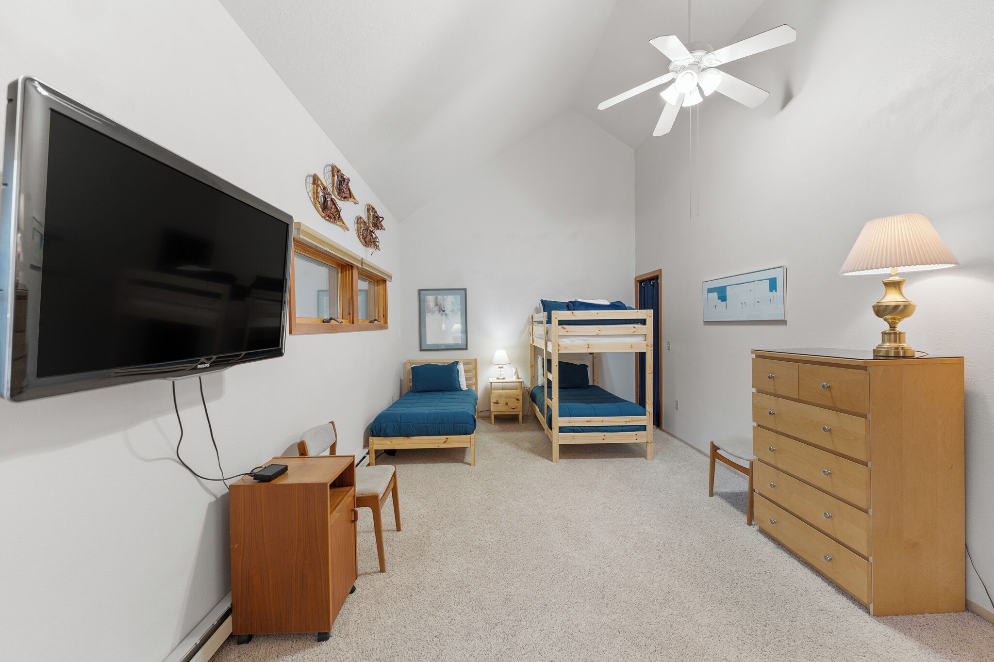A bedroom with a TV, bunk beds, a desk, a dresser, and a ceiling fan.