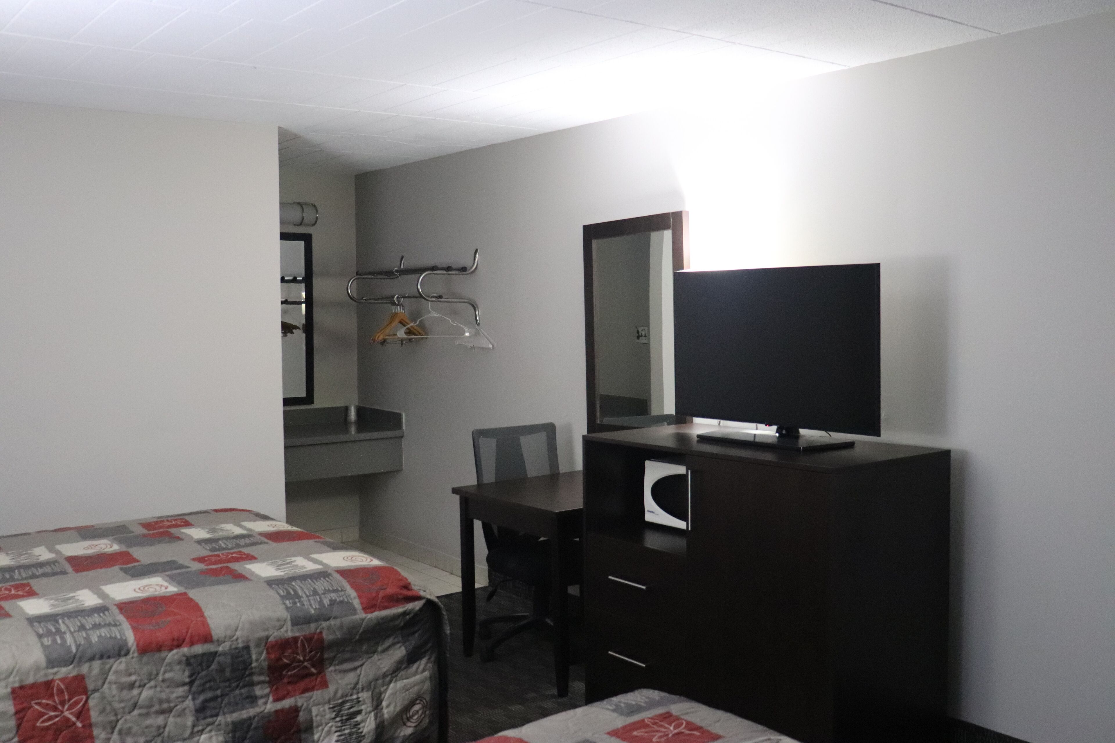 A hotel room with a bed, a desk with a chair, a dresser, a mirror, and a television.