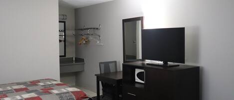 A hotel room with a bed, a desk with a chair, a dresser, a mirror, and a television.