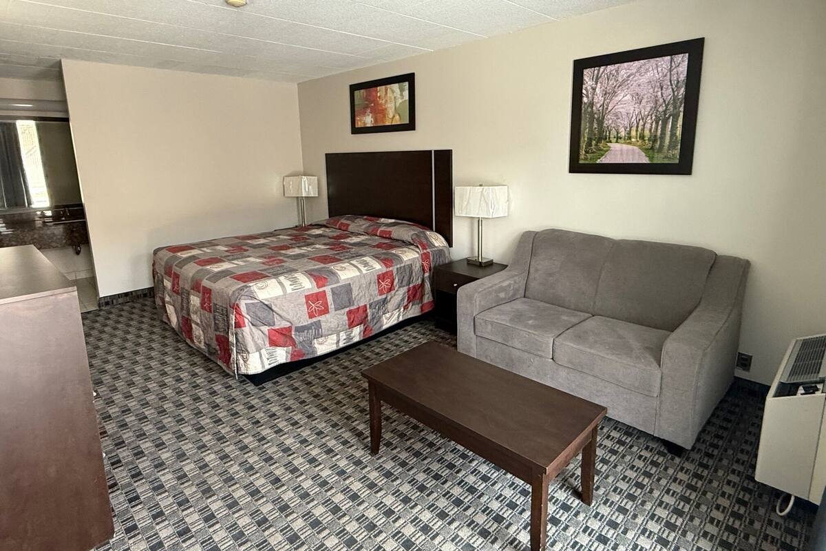 Una habitación de hotel con una cama, un sofá gris, una mesa de madera y dos lámparas de pared.