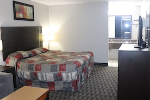 A hotel room with a bed, bedside tables, a desk, a chair, a lamp, a TV, a mirror, and a bathroom visible through an open door. - Fort York Motel (Mississauga)