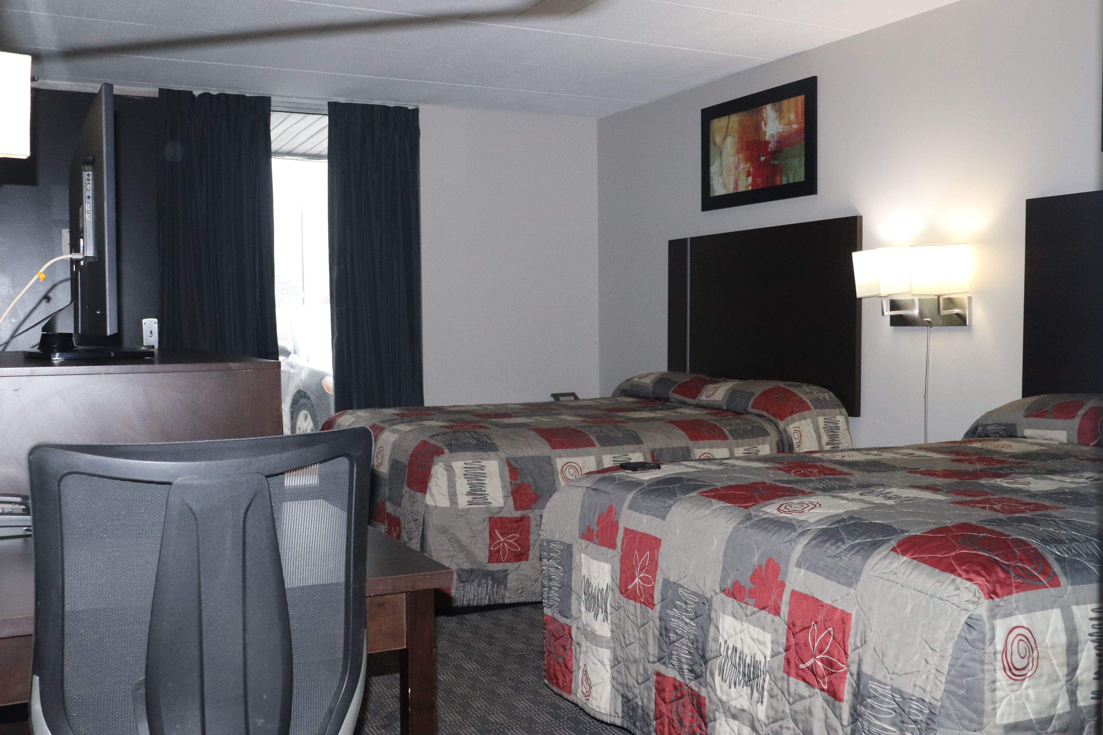A hotel room with two beds, a desk, a chair, a TV, and a painting on the wall.