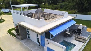 Un área de piscina moderna al aire libre con una zona de estar techada, un jacuzzi y un solárium junto a la piscina.