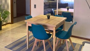 Een eetruimte met een houten tafel, blauwe stoelen, een potplant en een aan de muur bevestigde televisie.