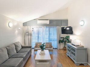 Ein modernes Wohnzimmer mit einem grauen Sofa, einem Couchtisch, einem Fernseher und einer Pflanze.