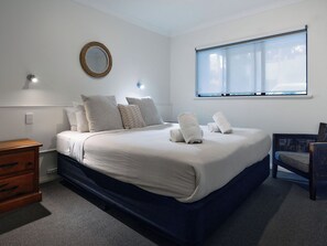 Ein Hotelzimmer mit einem Bett, einer Holzkommode, einem Sessel, einem Fenster und einem Wandspiegel.