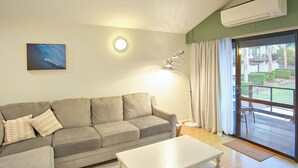 Ein Wohnzimmer mit grauem Sofa, einem weißen Couchtisch, einem Bild an der Wand und einem großen Fenster mit Vorhängen.