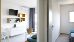 A modern, well-lit room with a white wall, a flat-screen TV mounted above a white cabinet, a small table with a basket, and a blue sofa.