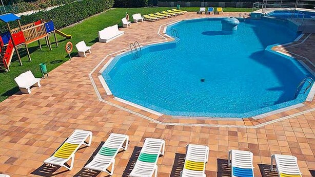 A swimming pool with a tiled deck, surrounded by lounge chairs and a children's play area.