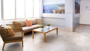 A reception area with a sofa, a wicker chair, a wooden coffee table, and a potted plant. A large window offers a view of the sea and cliffs. - APCOSTAS Estartit Confort / One Bedroom (L'Estartit)