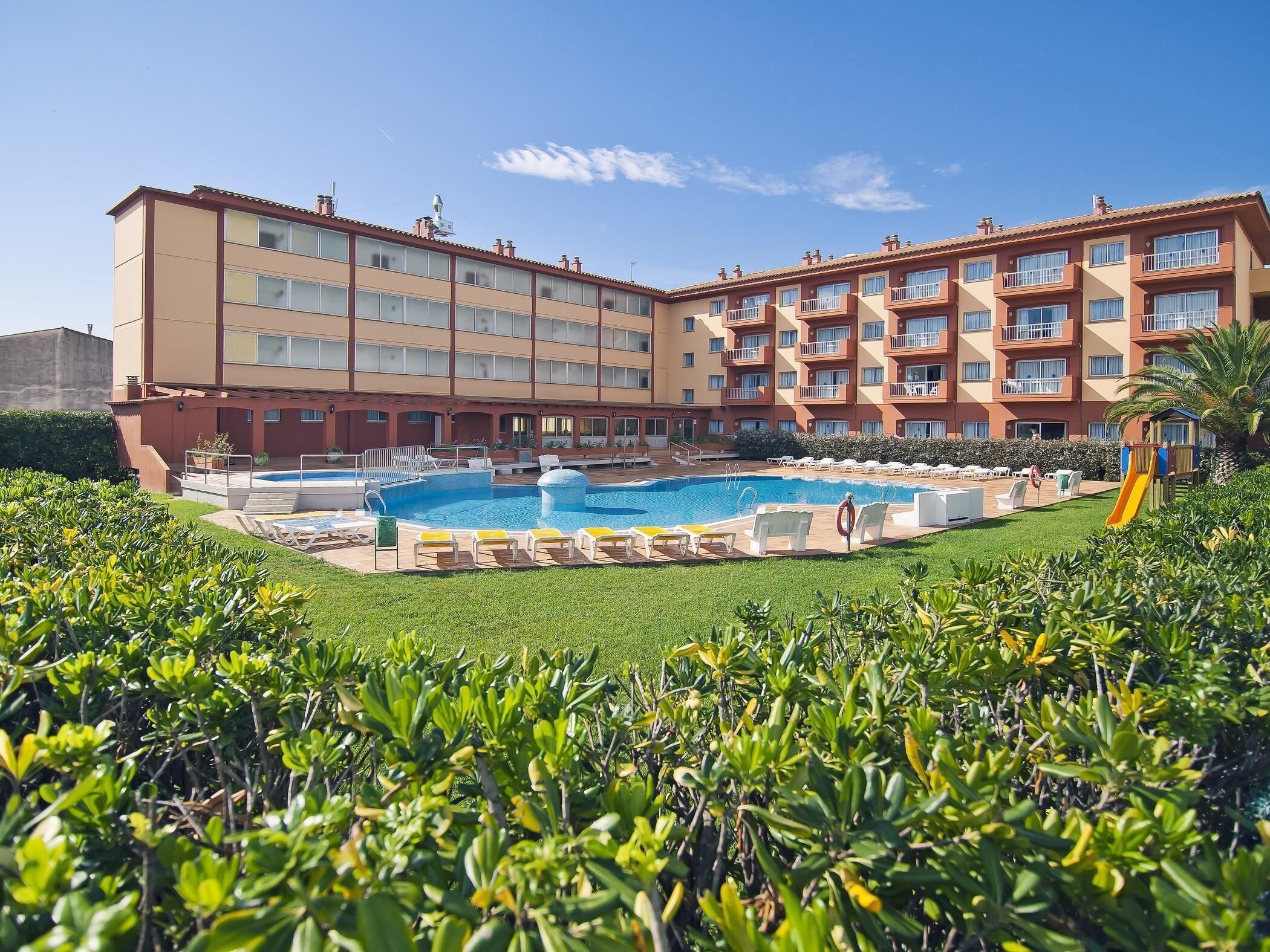 A hotel with a swimming pool, multiple balconies, and a playground.