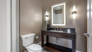 Une salle de bain comprenant des toilettes, un lavabo, un miroir et deux appliques murales.