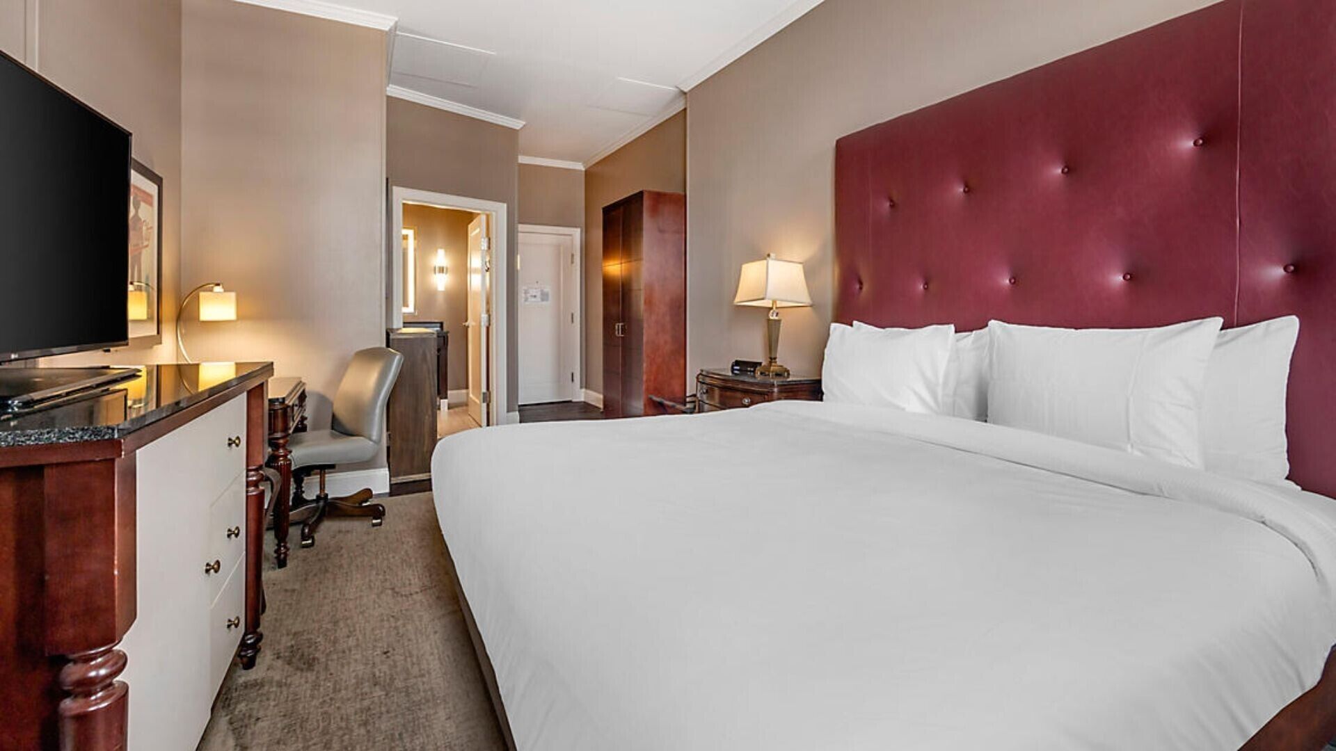 Habitación de hotel con una cama grande, televisión, escritorio con silla y espejo.