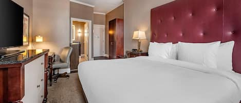 Une chambre d’hôtel avec un grand lit, une télévision, un bureau avec une chaise et un miroir.