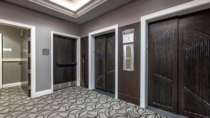 A hallway with patterned carpet, dark wooden doors, and a light fixture on the ceiling.