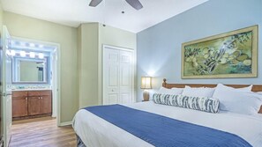 Ein Schlafzimmer mit einem großen Bett, einem Nachttisch mit Lampe, einer Kommode und einem Spiegel.