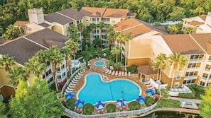 Ein Resort mit einem zentralen Schwimmbad, mehreren Balkonen und üppiger Bepflanzung.