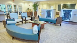 Eine geräumige Lobby mit einem gebogenen, blauen Sofa, mehreren Sesseln, einem Couchtisch und einem Empfangsbereich.