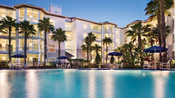 Ein Hotel mit Poolbereich, Palmen und Sitzgelegenheiten im Freien.