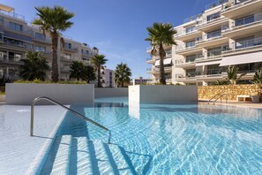 Una piscina con agua azul cristalina, rodeada de palmeras y edificios de apartamentos modernos.