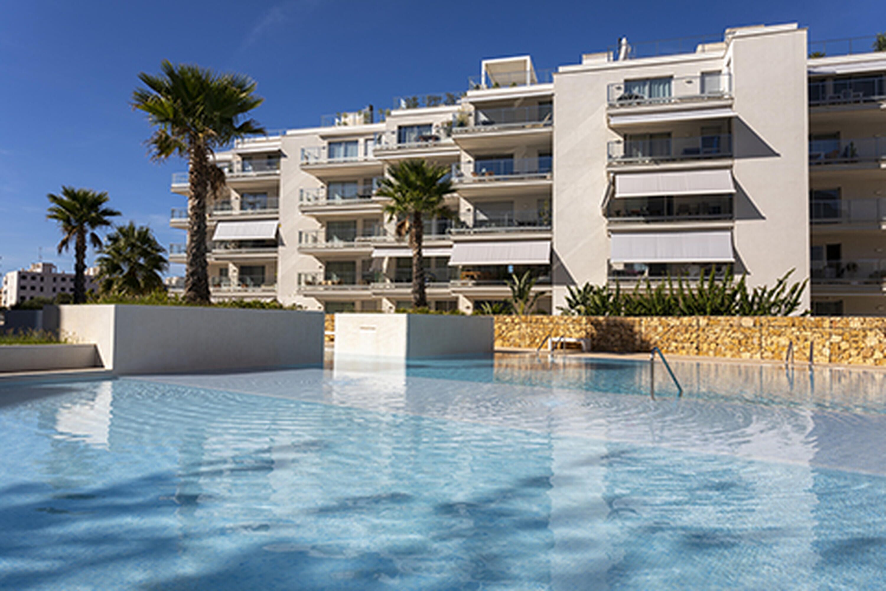 Una piscina rodeada de edificios modernos con balcones y palmeras.