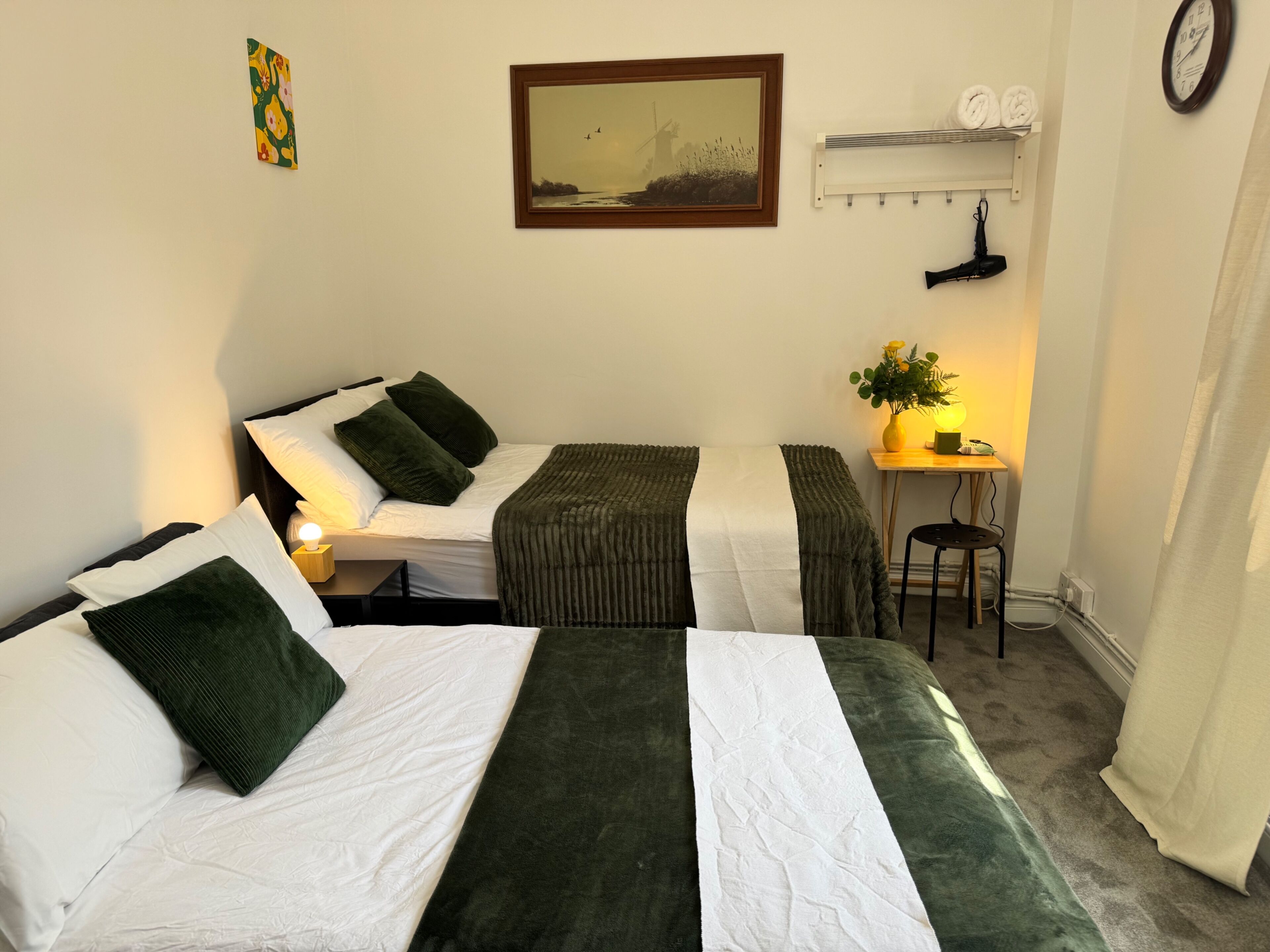 Une chambre avec deux lits, une petite table avec une lampe, une horloge et un tableau au mur.
