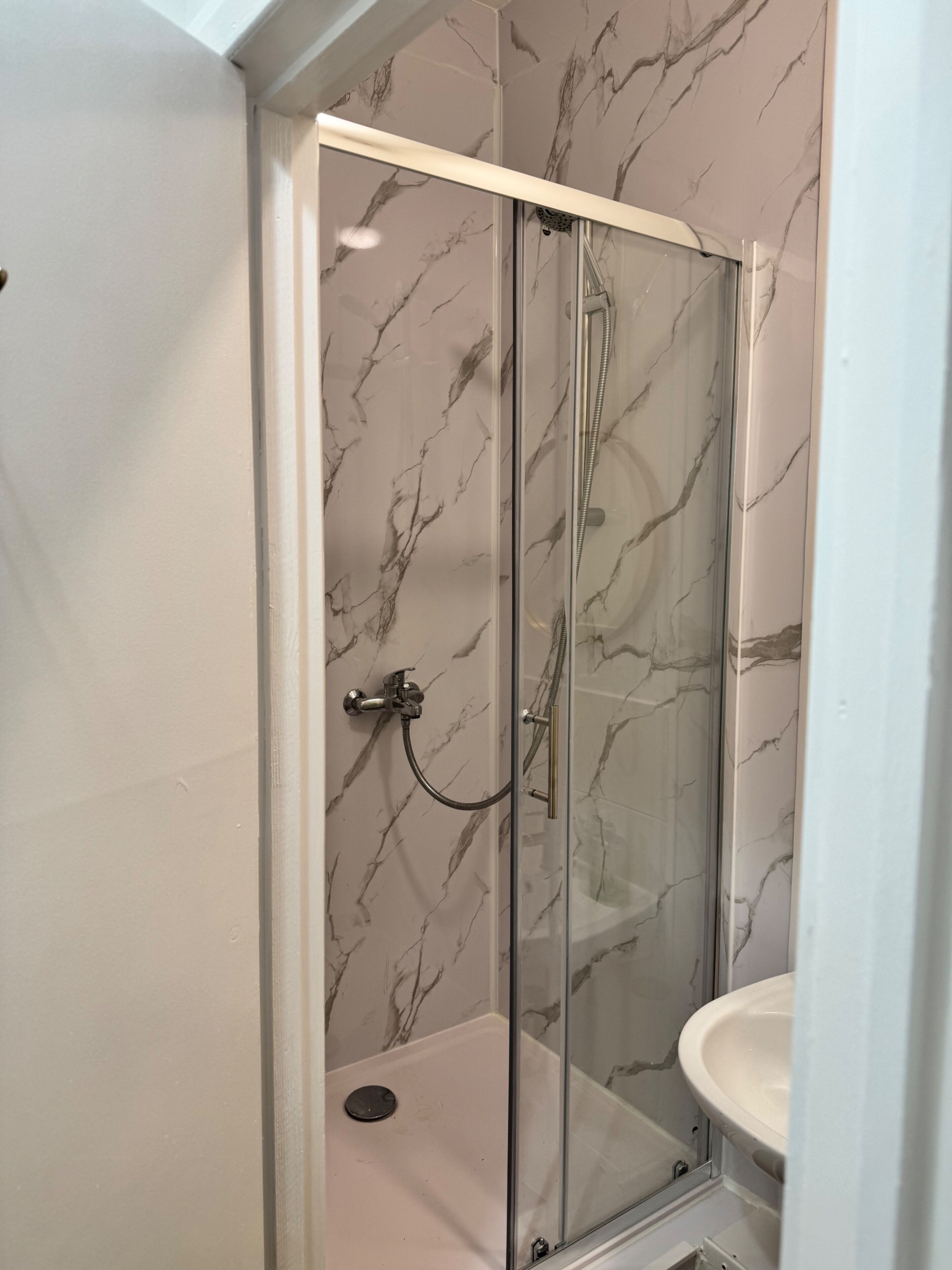 A glass-enclosed shower with a marble-patterned wall, a sink, and a showerhead.
