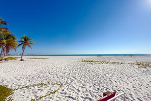 A beach with white sand, palm trees, and a clear blue sky.