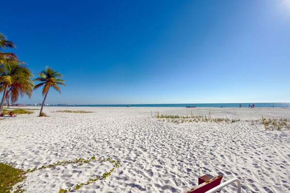 Una playa de arena blanca, palmeras y un cielo azul despejado.