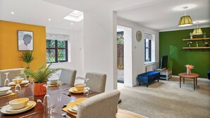 Un coin repas avec une table en bois dressée pour quatre personnes, une plante en pot et un luminaire suspendu moderne.