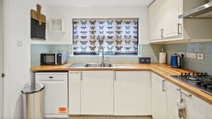 Une cuisine avec des armoires blanches, un plan de travail en bois, un four à micro-ondes, un évier, une cuisinière et une fenêtre ornée d’un motif de papillons.