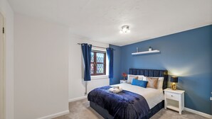 Une chambre à coucher avec un grand lit, une table de chevet, une fenêtre avec des rideaux et une étagère au-dessus du lit.