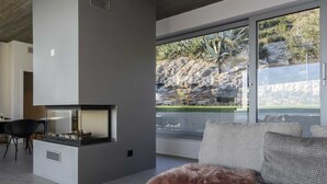 En moderne stue med pejs, sofa og et stort vindue med udsigt over et stengrundt landskab.